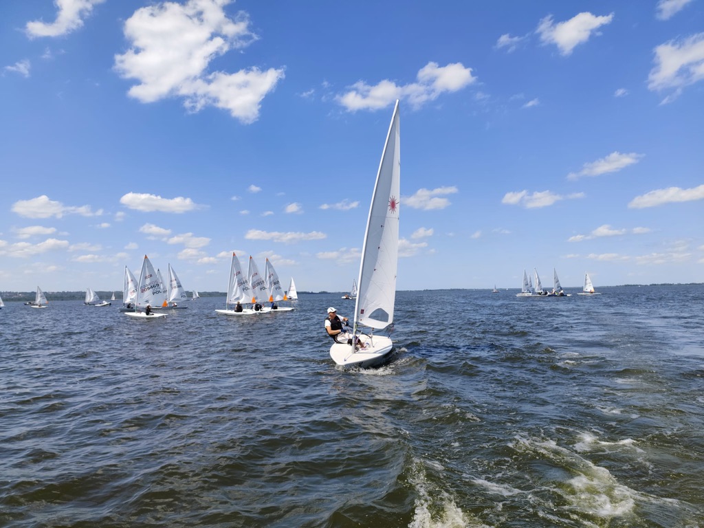 Żeglarz na łodzi ILCA na tle floty w tle