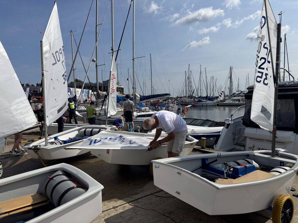 Zawodnicy szykujący łódki optimist na marinie